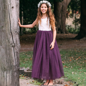 Young girl in a purple dress standing next to a tree in a natural setting