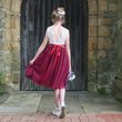 Girl in a red and white dress standing in front of a stone wall.