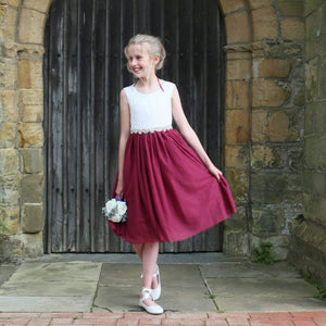 Young girl in a white top and red skirt standing in front of a stone wall.