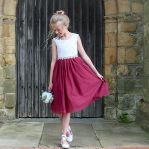Young girl in a white top and red skirt standing in front of a stone wall.