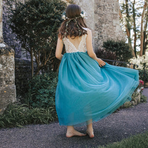 Woman in a turquoise teal dress with a floral headpiece standing in front of a stone building.