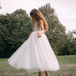 girl in a white dress standing in a park with trees in the background