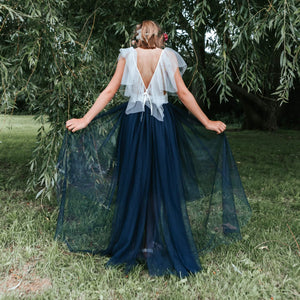 Girl in a blue and white dress standing in a grassy area with trees.
