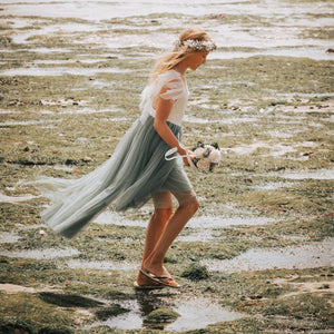 Girl in a flowing dress from UK Flower Girl Boutique walking on a beach with a bouquet.