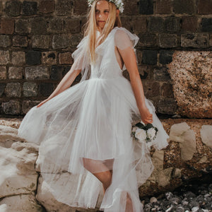 girl in a white dress standing against a stone wall.