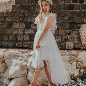 Young girl in a white dress standing against a stone wall.