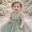 Child in a green dress with a flower crown standing in front of white flowers