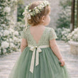 Child in a green dress with a floral headband standing in a garden setting.