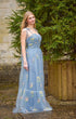 Woman in a blue floral dress standing outdoors with greenery in the background