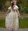 Young girl in a floral dress standing by a pond with greenery in the background