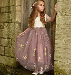 Young girl in a floral dress standing against a stone wall