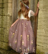 Young girl in a floral dress standing against a stone wall.