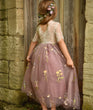 Young girl in a floral dress standing against a stone wall.
