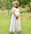 Young girl in a white floral dress standing in a grassy field with trees in the background