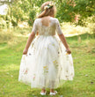 Girl in a floral dress standing in a grassy field with trees in the background