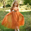 Young girl in an orange dress standing in a grassy field with trees in the background