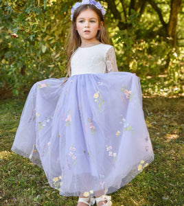 Young girl in a white top and light purple skirt with floral embroidery standing outdoors.