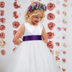 Girl wearing s white flower girl dress with purple sash