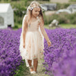 A young girl wearing a light pink floral dress and a flower crown walks through a field of purple lavender.