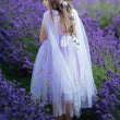 A young girl standing in a field of purple lavender, wearing a white tulle dress with a matching sheer veil and floral hair accessories.