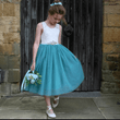 Young girl in a white and dress  holding flowers against a stone wall.