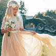 A young girl wearing a two-piece lace and tulle dress, holding a bouquet of white flowers. The dress features a white lace short-sleeve bodice with a white waistband and a flowing pale peach-pink tulle skirt.