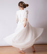 Girl in a white skirt and top with lace sleeves and a flowing skirt on a plain background