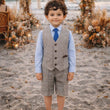 Child in formal attire standing on a beach with floral arches and a sunset in the background
