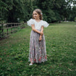 Young girl in a floral dress standing in a grassy field with trees in the background