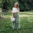 Young girl in a green dress standing in a park with trees in the background