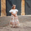 Young girl in a floral dress standing in front of large doors.