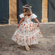 Girl in a floral dress walking away from the camera in front of a brick building.