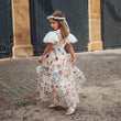 Young girl in a floral dress standing in front of a brick building.