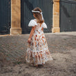 Girl  in a floral dress standing in front of a brick building with arched doors.