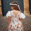 Young girl in a floral dress with a white headband standing in front of a large door.