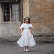 Young girl in a white dress standing in front of a stone building