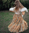 child in a vintage dress with a floral pattern standing outdoors.
