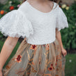 Child wearing a white lace top and floral skirt with a garden background