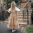 Child in a floral dress walking away from a stone building with steps.