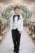 Young boy in a formal outfit walking down a decorated wedding aisle with flowers and candles.