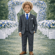 Child in a gray suit standing in front of floral decorations at an outdoor event.