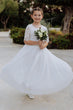 Young girl in a white dress holding flowers outdoors