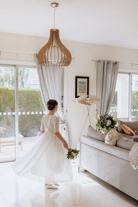 Woman in a white dress standing in a modern living room with large windows.