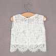 White lace vest on a wooden hanger against a gray background