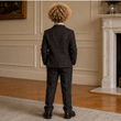 Person wearing a dark plaid suit standing in a room with a fireplace.
