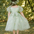 Child wearing a light green dress with floral embroidery in a natural setting