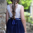 Girl wearing a white lace top and navy blue skirt with a blurred natural background