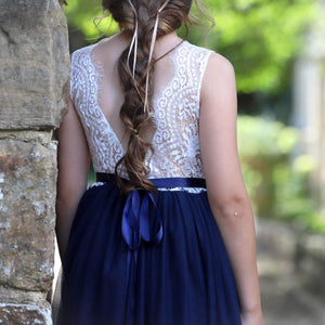 Girl wearing a white lace top and navy blue skirt with a blurred natural background