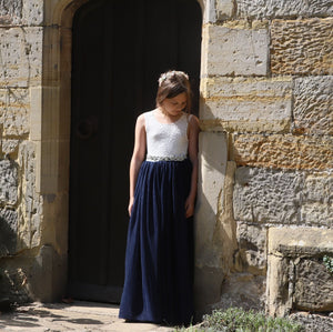 Girl in a white top and navy blue skirt standing against a stone wall.