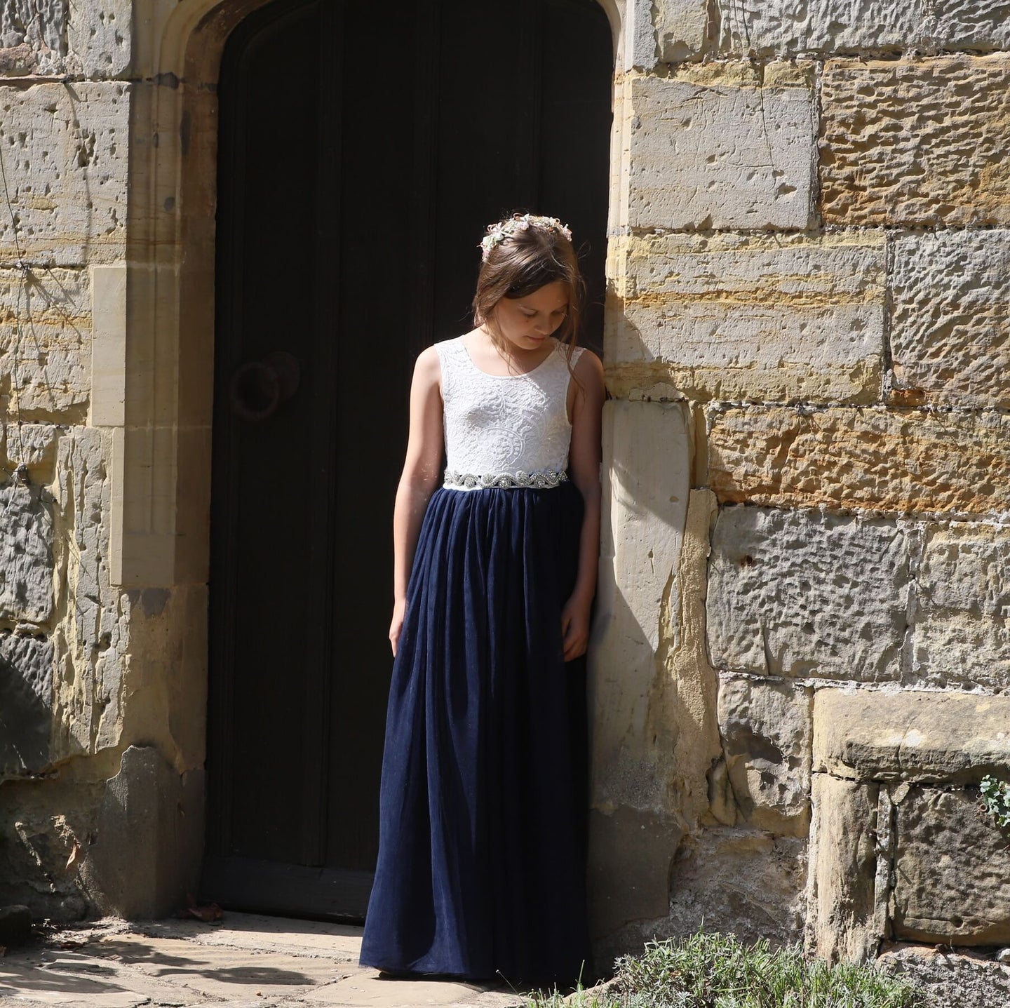 Girl in a white top and navy blue skirt standing against a stone wall.